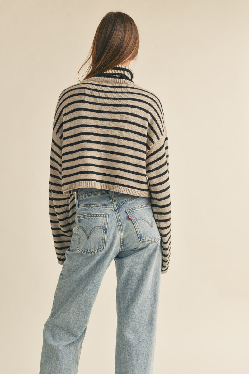 back view of the model wearing the jenny striped sweater top. shows the black stripes. also shows the turtleneck, the dropped shoulders, the cropped length and the ribbed detailing. 