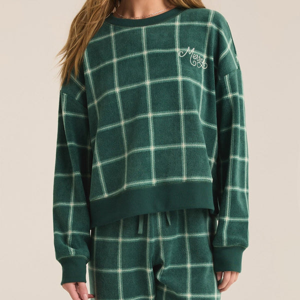 front view of the model wearing the plaid long sleeve top. shows the word merry in the left corner. also shows the dropped shoulders, the crew neckline, the relaxed fit and the green and white plaid. 