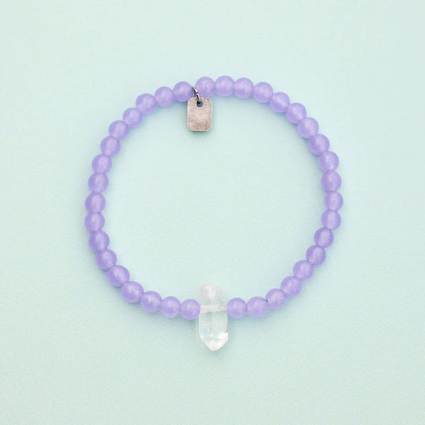 Shows bracelet on a flat surface. Purple amethyst beads with raw clear quartz center crystal.