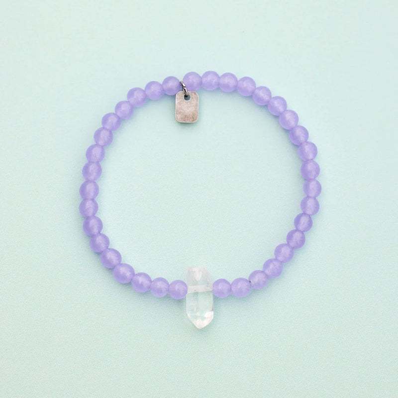 Shows bracelet on a flat surface. Purple amethyst beads with raw clear quartz center crystal.