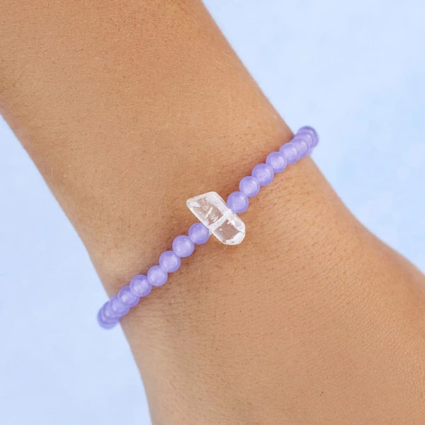 Shows stretch bracelet on models wrist. Features purple amethyst beads with a clear raw quartz stone in center.