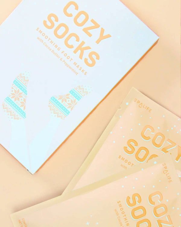 picture of the cozy socks packaging. on the packaging it says cozy socks, smoothing foot masks with cocoa butter & peppermint. shows the print of the foot masks. 