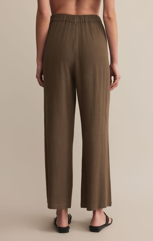 back view of the model wearing the vista pant. shows the high rise waist. also shows the brown color, the full length and the slight cinched at the waist. 