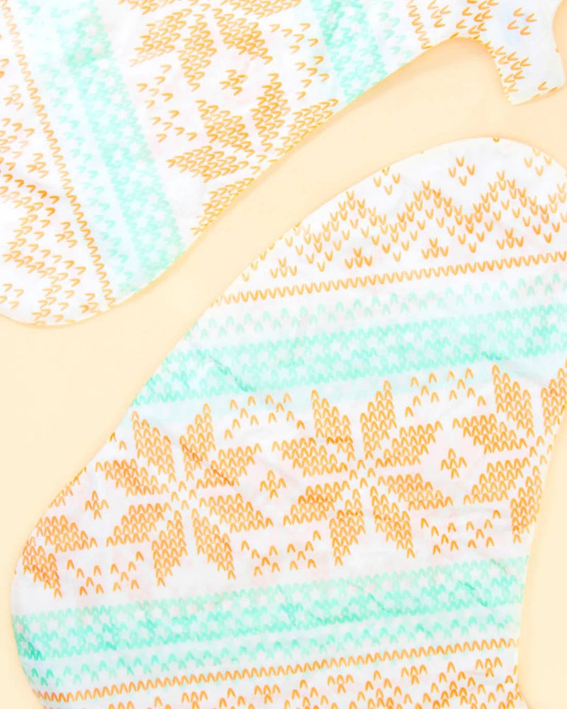 shows the snowflake print of the foot masks. The colors are orange and mint. 