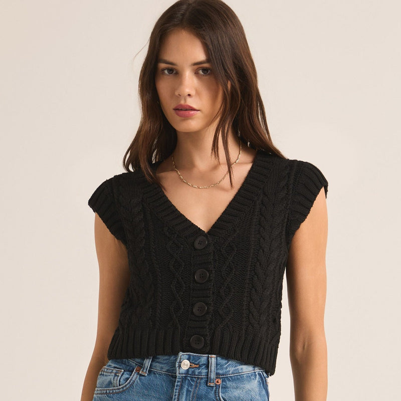 front view of the model wearing the set adrift sweater vest. shows the cap sleeves. also shows the front button closure, the cropped length and the cable knit detail throughout. 