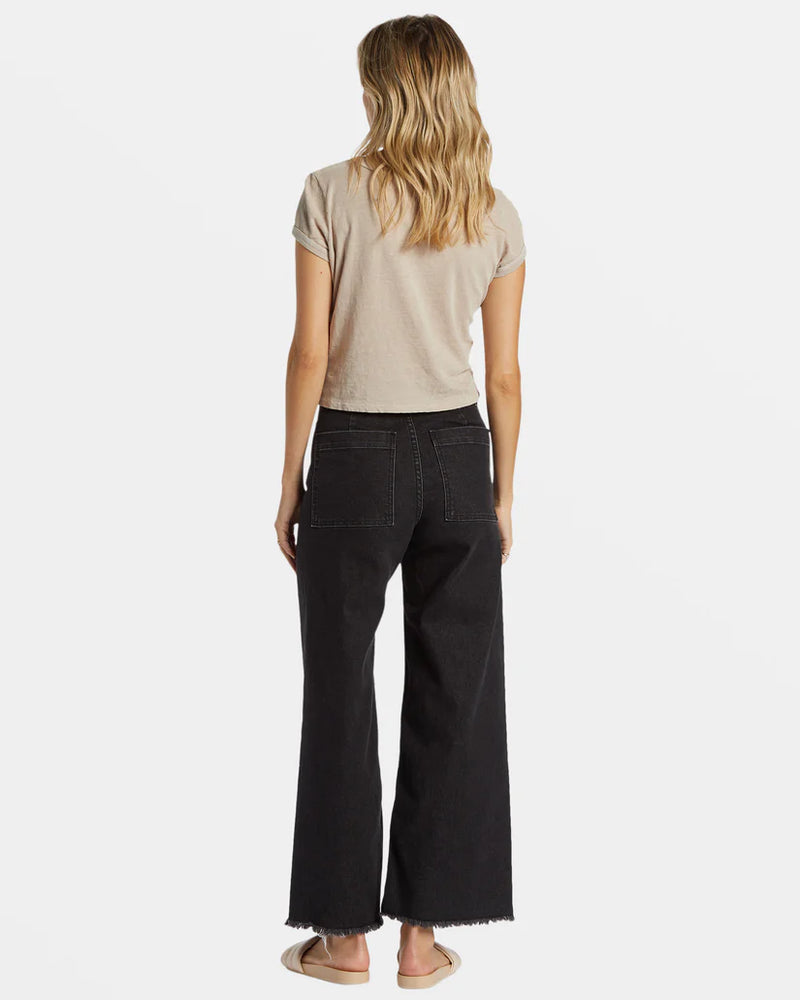 back view of the model wearing the free fall high waist pants. shows the patch pockets. also shows the wide leg, the bottom frayed raw hem and the black rinse color. 