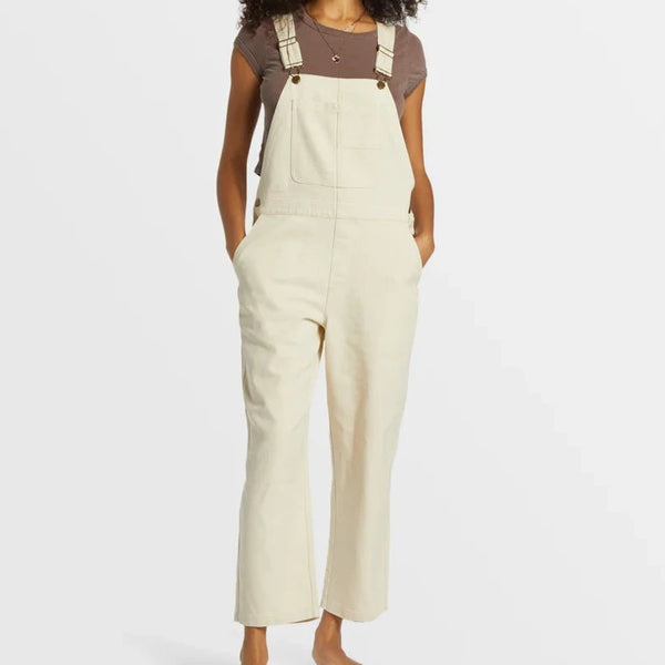 front view of the model wearing the sand canyon denim overalls. shows the adjustable straps. also shows the relaxed fit, the multiple pockets, the side button closure, and the slight flare bottoms. 