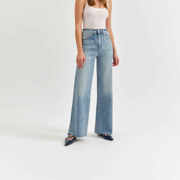 front view of the model wearing the far out high rise wide leg jean. shows the high rise waist. also shows the wide leg, the raw bottom hem and the lighter wash. 