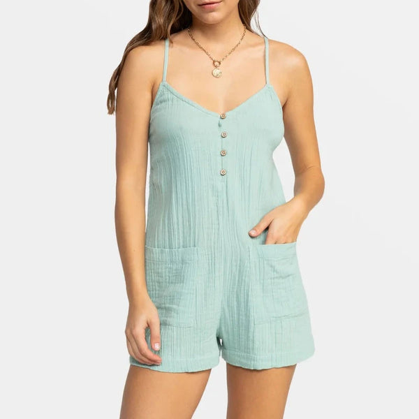 front view of the model wearing the sunshine haze v neck romper. shows the v neckline. also shows the front coconut button closure, the front patch pockets and the skinny straps. 