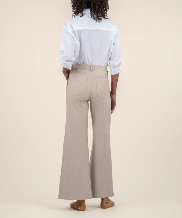 back view of the model wearing the meg high rise wide leg trousers in stone. shows the patch pockets. also shows the wide legs, the belt loops and the high rise waist. 