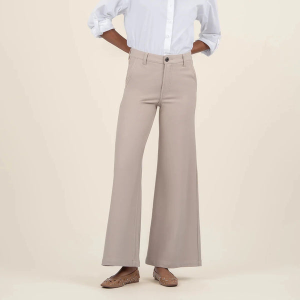 front view of the model wearing the meg high rise wide leg trousers in stone. shows the high rise waist. also shows the wide leg, the stone color, the button closure and the belt loops. 