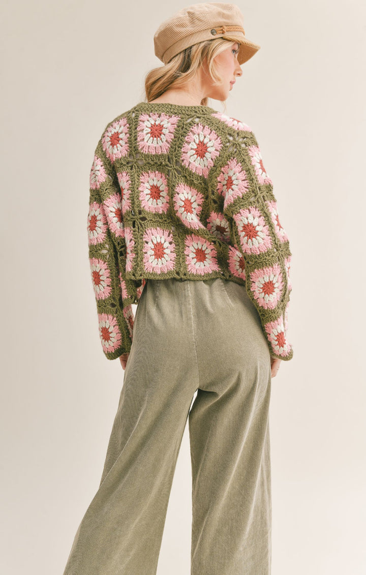 Back view of model wearing the crochet cardigan. Shows the crochet daisy print. Also shows the cropped length with the long sleeves.