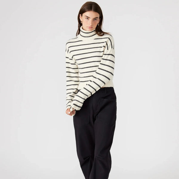 front view of the narsha sweater. shows the dropped shoulders. also shows the turtleneck, the bell flare sleeves, and the striped pattern. 