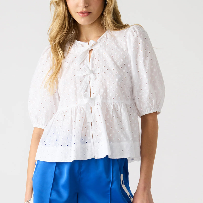 front view of the model wearing the paula top. shows the tie front detail. also shows the puff short sleeves, the eyelet detail and the white color. 