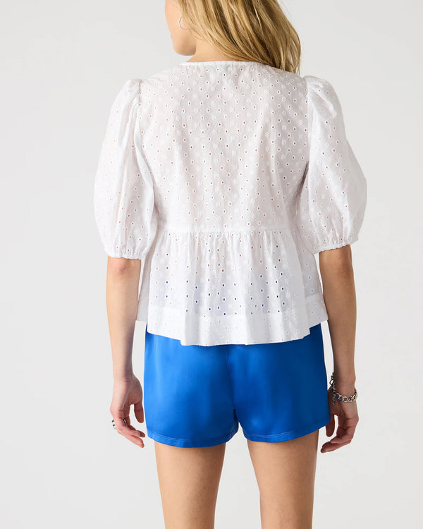 back view of the model wearing the paula top. shows the puff sleeves. also shows the white color, the peplum detail and the eyelet detailing. 