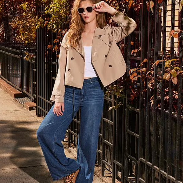 model stands with one leg propped and leaning against a fence, jeans are shown to be wide and flowing from the knee down