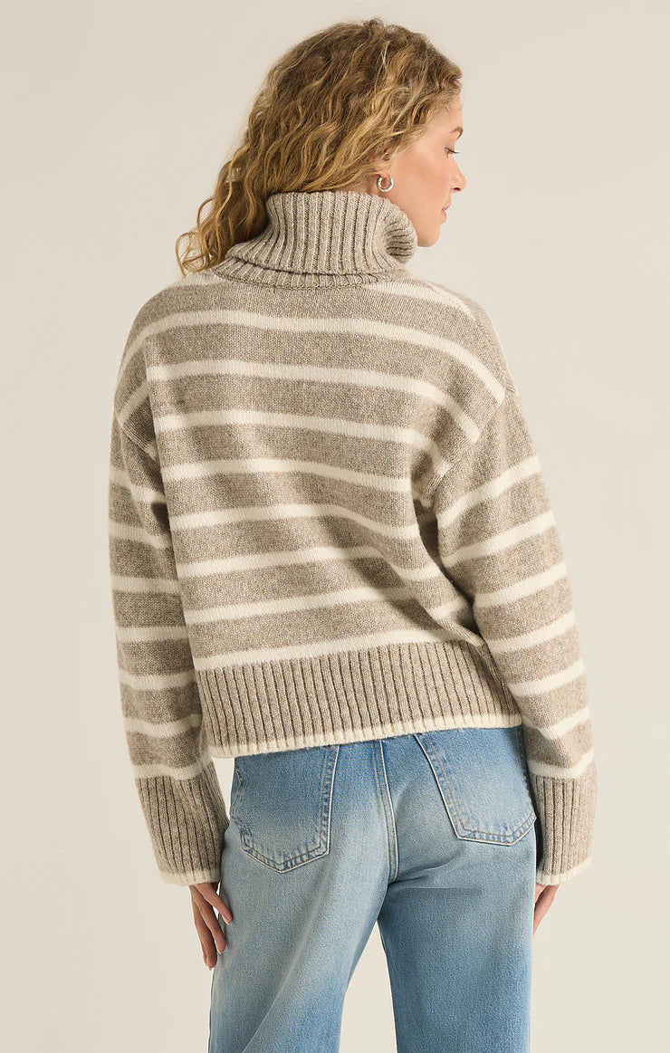 back view of the model wearing the josephine striped sweater. shows the ribbed detailing. also shows the dropped shoulders, the turtleneck and the tan and cream stripes. 