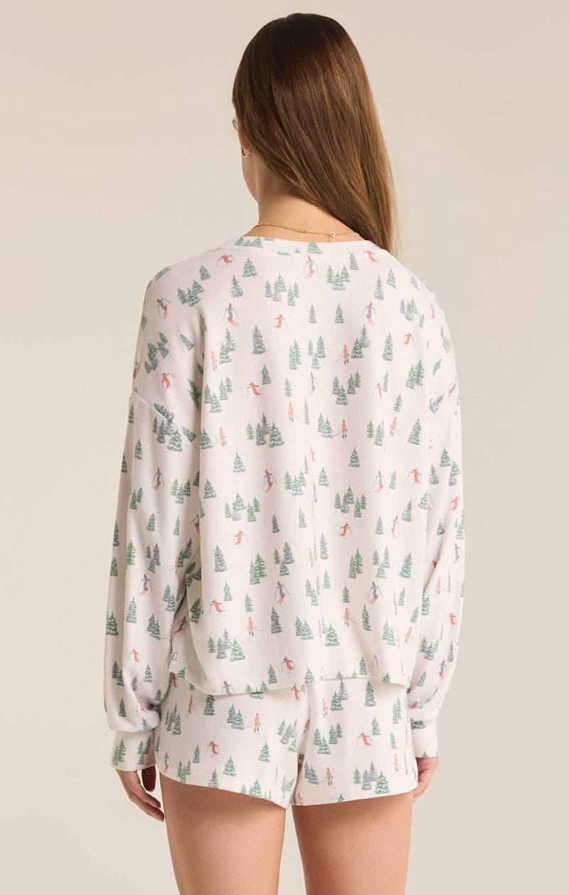 back view of the model wearing the alpine long sleeve. shows the dropped shoulders. also shows the long sleeves, the relaxed fit and the trees and skiers print. 