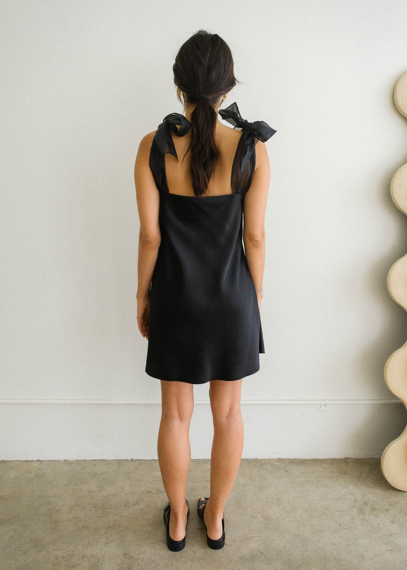 Back view of model wearing the Kate mini dress. Shows the mini dress with the square backing. It also shows the exaggerated bow tie straps.