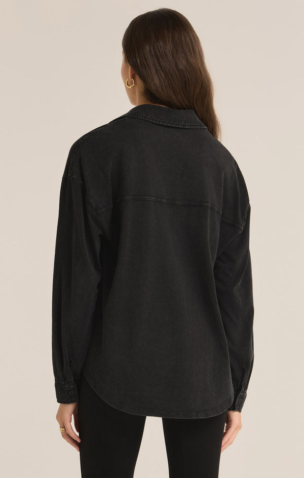 back view of the model wearing the niccola button up top in black. shows the collared neckline. also shows the dropped shoulders, the defined seaming throughout and the curved bottom shirttail detail. 