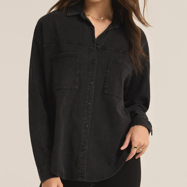 front view of the model wearing the niccola button up top in black. shows the button up front closure. also shows the two front patch pockets, the collared neckline and the curved bottom hemline. 