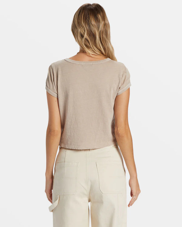 back view of the model wearing the daily tee. shows this beautiful light brown/beige color. also shows the crew neckline, the cropped length, the fitted style and the ribbed detailing on the sleeves and neckline. 