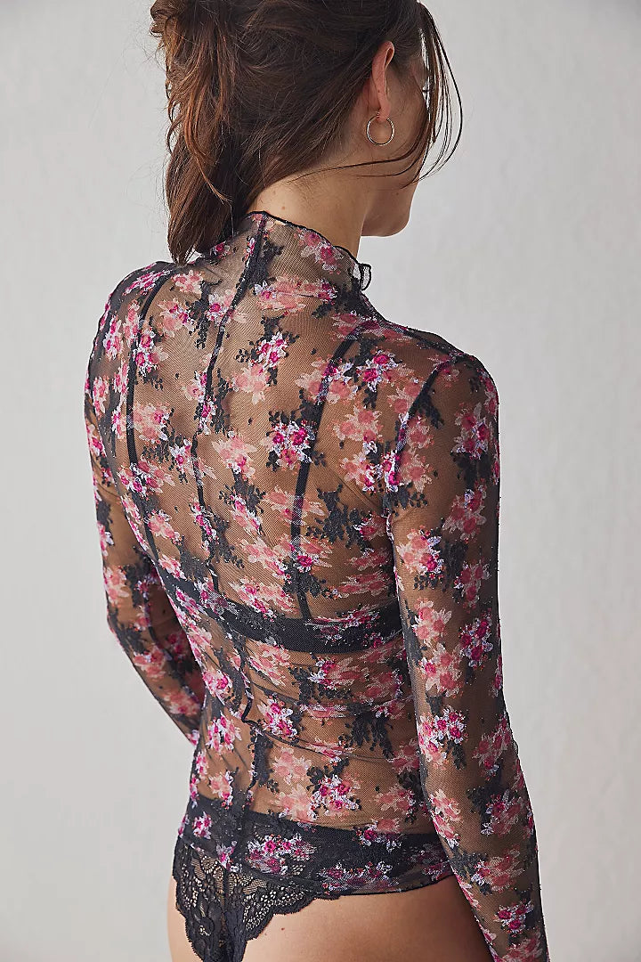 back view of the model wearing the lady lux layering top. shows the high neckline. also shows the printed and embroidered floral, the exposed seaming and the fitted sleeves. 