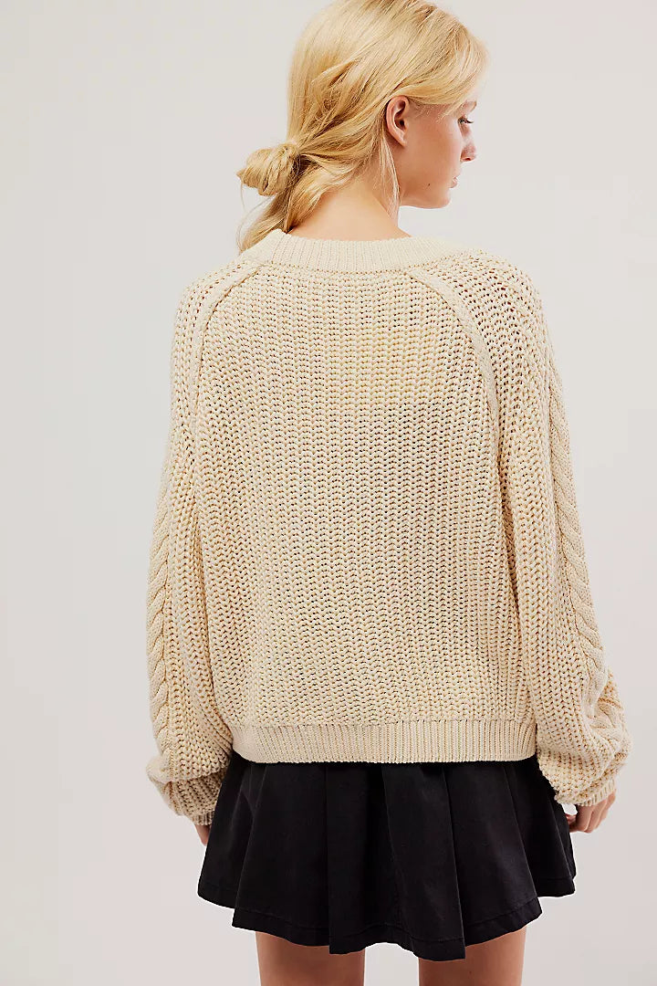 back view of the model wearing the frankie cable sweater. shows the oversized fit. also shows the sweater is in ivory the ribbed hems and the scoop neckline. 