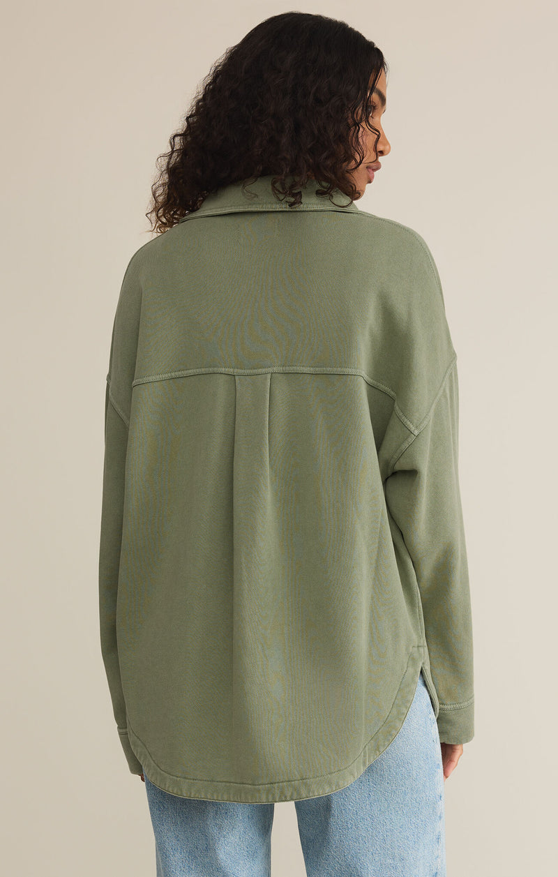 back view of the model wearing the all day knit jacket in avocado. shows the curved hem. also shows the collar, the exposed seaming and the dropped shoulders. 