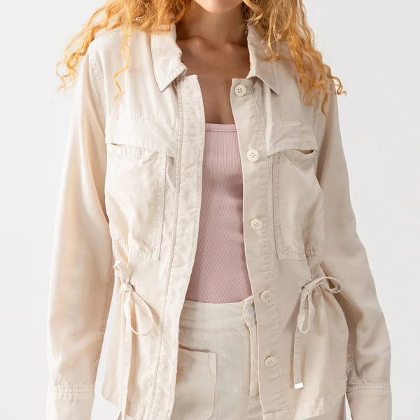 front view of the model wearing the lora surplus jacket. shows the waist drawstring. also shows the front button down closure, the traditional collar and the two front patch pockets. 