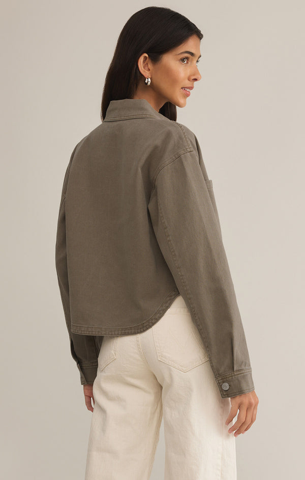 back view of the model wearing the all day cropped denim jacket. shows the curved bottom hem. shows the color, also shows the brownish color, the button in the sleeves. 