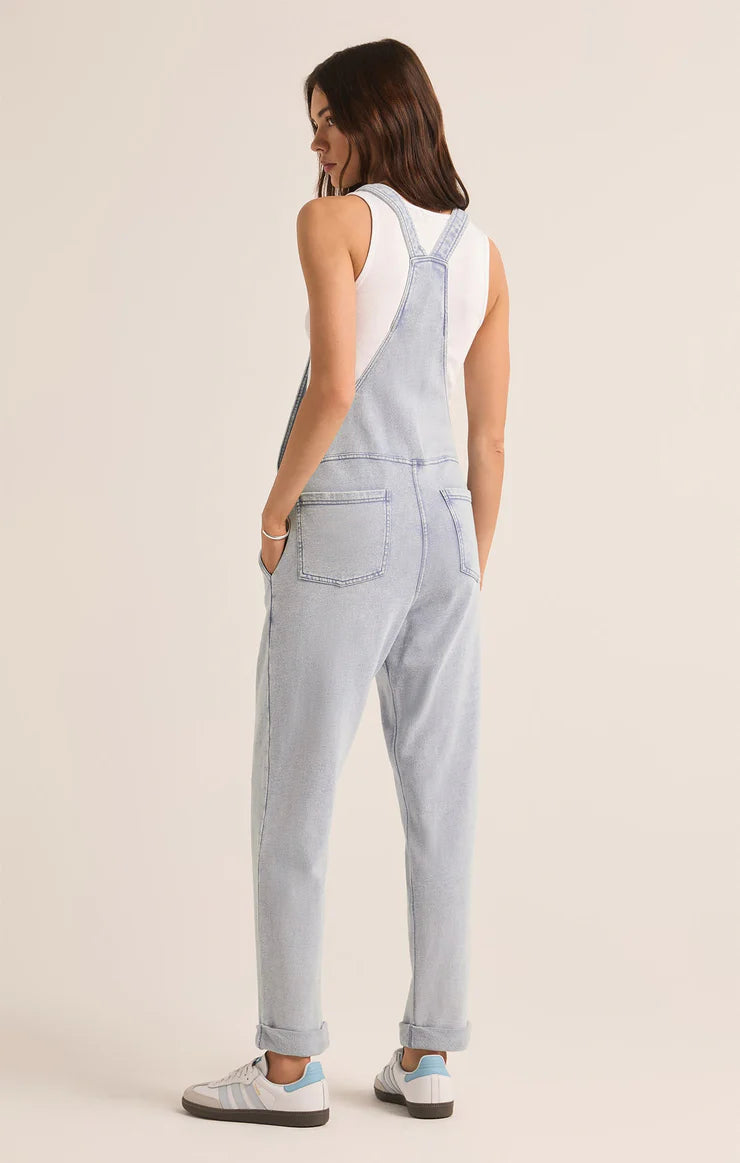 back view of the model wearing the knit denim overalls. shows the rolled bottom cuff. also shows the back pockets, and the side pockets. 