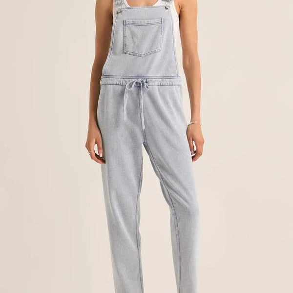 front view of the model wearing the knit denim overalls. shows the drawstring waist. also shows the front patch pouch, also shows the snap closure to the overalls. 