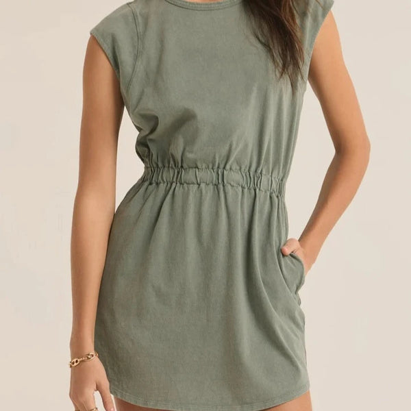 front view of the model wearing the Paxton jersey mini dress in palm green. shows the cap sleeves. also shows the smocked waistband, the bottom curved hem and the crew neckline. 