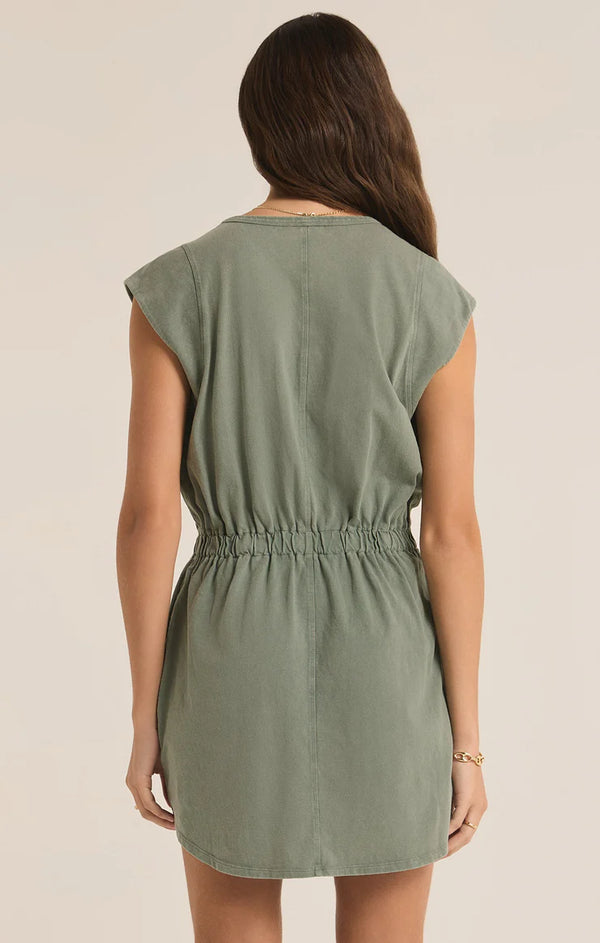 back view of the model wearing the paxton jersey mini dress in palm green. shows the smocked waistband. also shows the cap sleeves, the bottom curved hem and the defined seam detail throughout. 