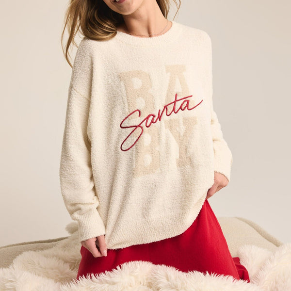 front view of the model wearing the santa baby cozy sweater. shows the wording on the front that says santa baby. shows the crew neckline, the ribbed detailing, and the soft fabric. 