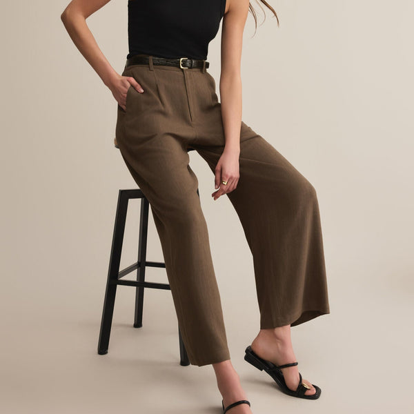 front view of the model wearing the vista pant. shows the side seam pockets. also shows the brown color, the high waist and the zip fly/button closure. 