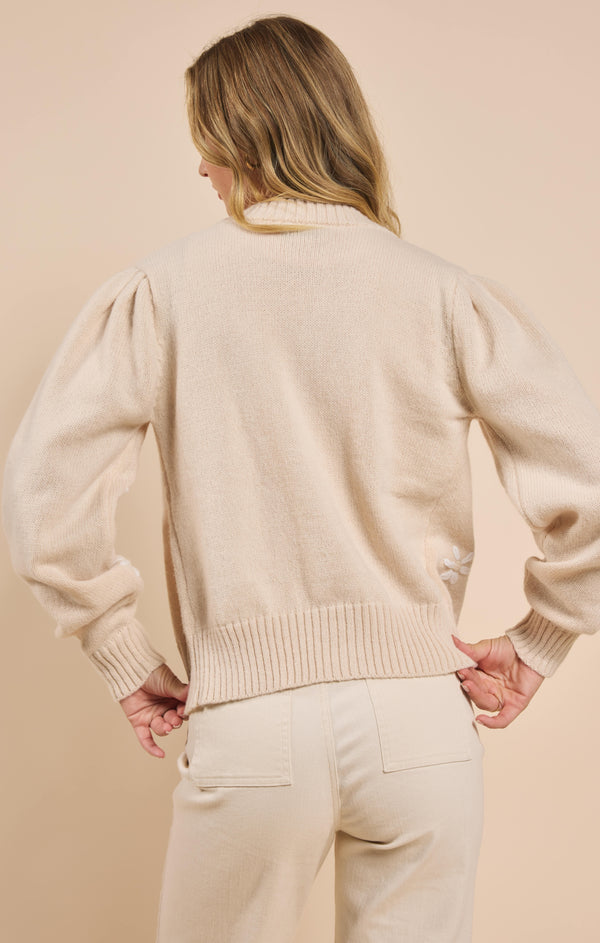 back view of the model wearing the pretty daisy cardigan. shows the ribbed hems. also shows the puff sleeve, and the cream color of the cardigan. 