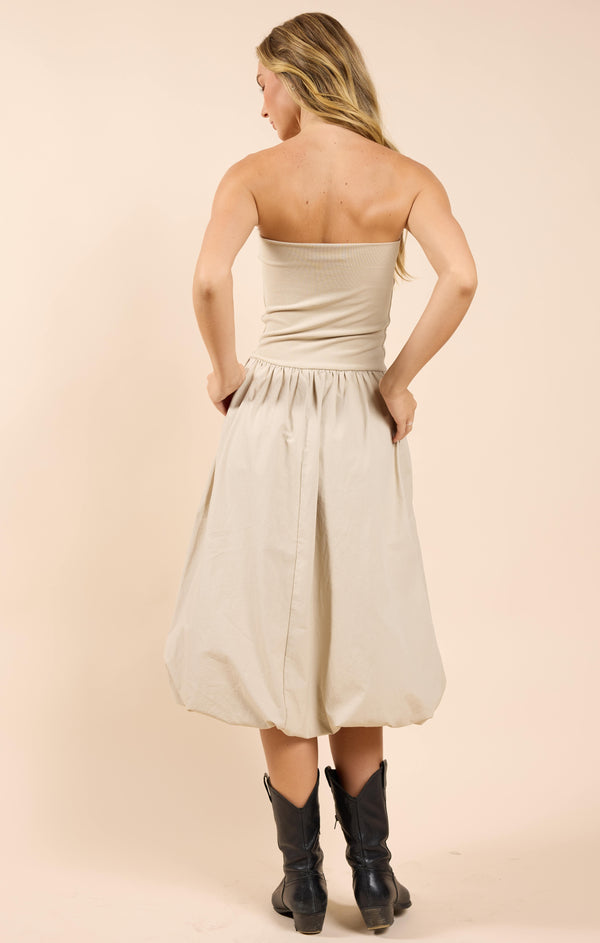 back view of the model wearing the happier now strapless bubble dress. shows the midi length. also shows that the dress is strapless, the bubble skirt and the beige color. 