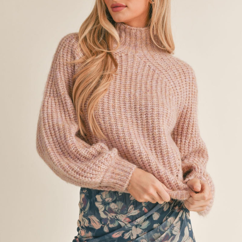 front view of model wearing Malory sweater in pink. shows the mock neck. also shows the dropped shoulders, the slight puff sleeves and the knit detailing throughout. 