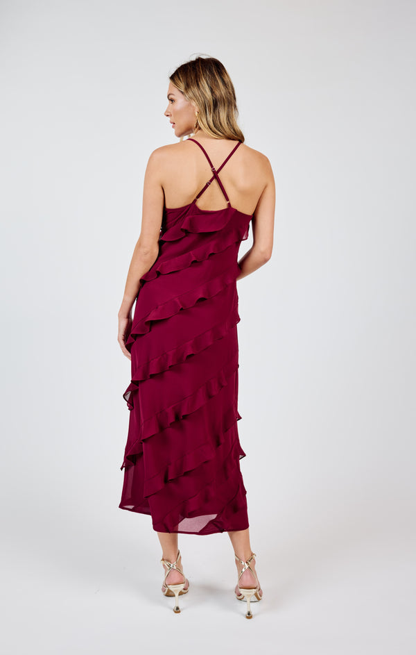 back view of the model wearing the all invited ruffle maxi dress. shows the criss cross straps. they are also adjustable. also shows the ruffle design and the midi length. 