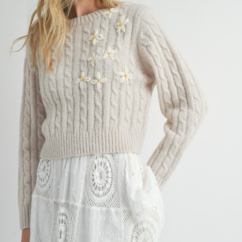 front view of the model wearing the lulu embroidered daisy sweater. shows the cable knit detail throughout. also shows the embroidered daisies on the front, the crew neckline and the ribbed detailing on the neckline, bottom hem and arm cuffs.  