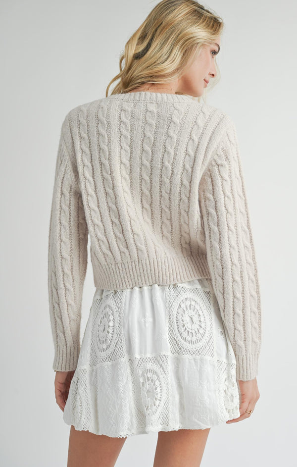 back view of the model wearing the lulu embroidered daisy sweater. shows the cropped length. also shows the cable knit detailing throughout, and the ribbed detailing on the neckline, bottom hem and the sleeve cuffs. 
