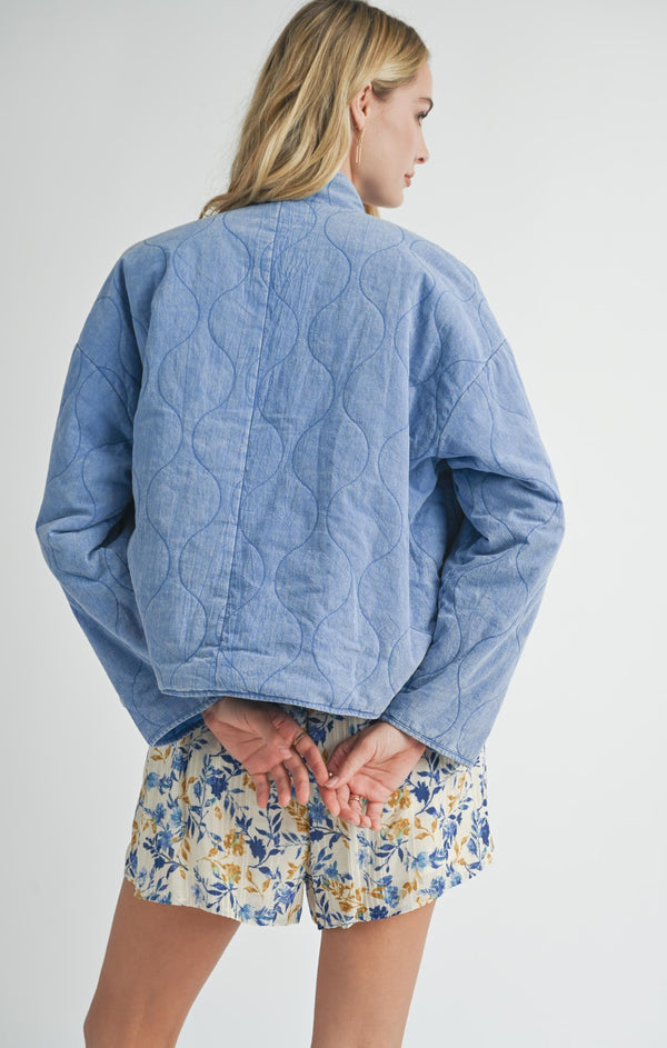 back view of the model wearing the weekender washed quilt jacket. shows the defined seaming going down the middle. also shows the dropped shoulders, the washed blue color and the quilt detailing throughout. 