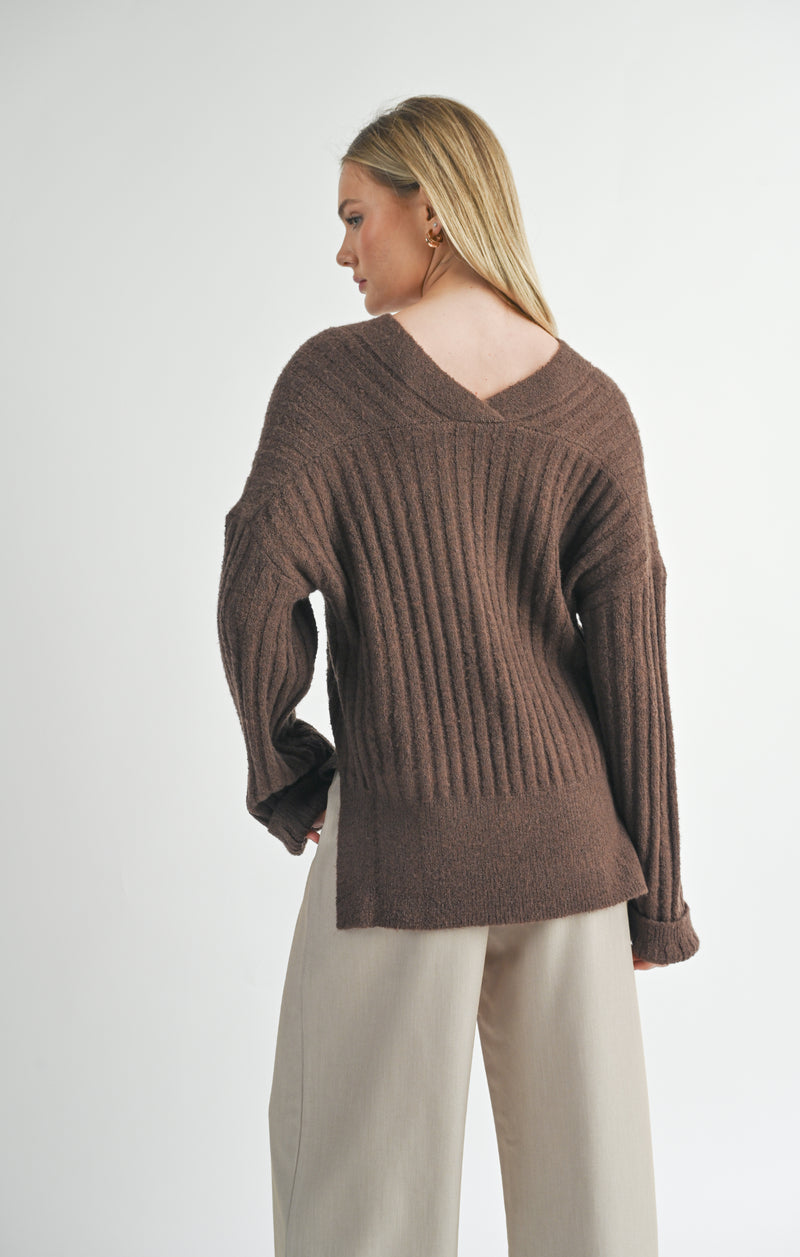 back view of the model wearing the carli v neck pullover. shows the side slits. also shows the dropped shoulders, the ribbed detailing and the oversized fit. 