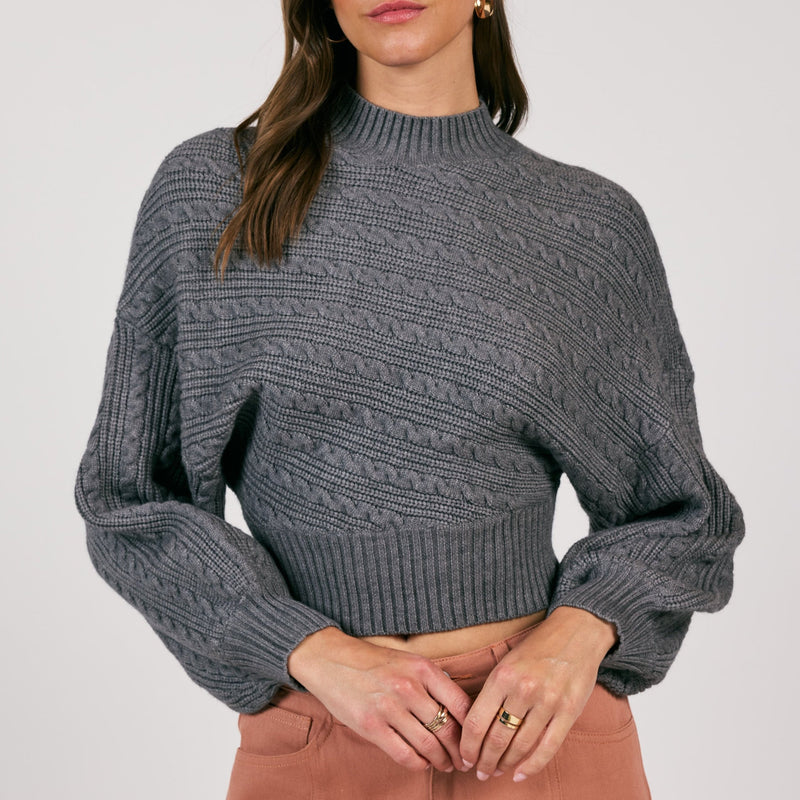 front view of the model wearing the along the vines cable knit sweater. shows the mock neckline. also shows the ribbed detailing on the hems, the exaggerated sleeves and the cable knit detailing throughout. 