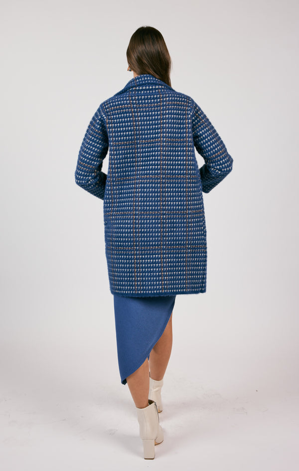 back view of the model wearing the marceau houndstooth coat. shows the mid length. also shows the traditional collar and the houndstooth design. 