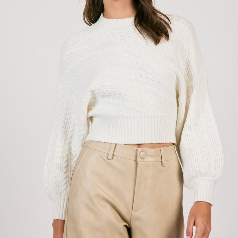 front view of the model wearing the along the vines cable knit sweater. shows the mock neckline. also shows the cropped length, the ribbed hems and the exaggerated sleeves. 