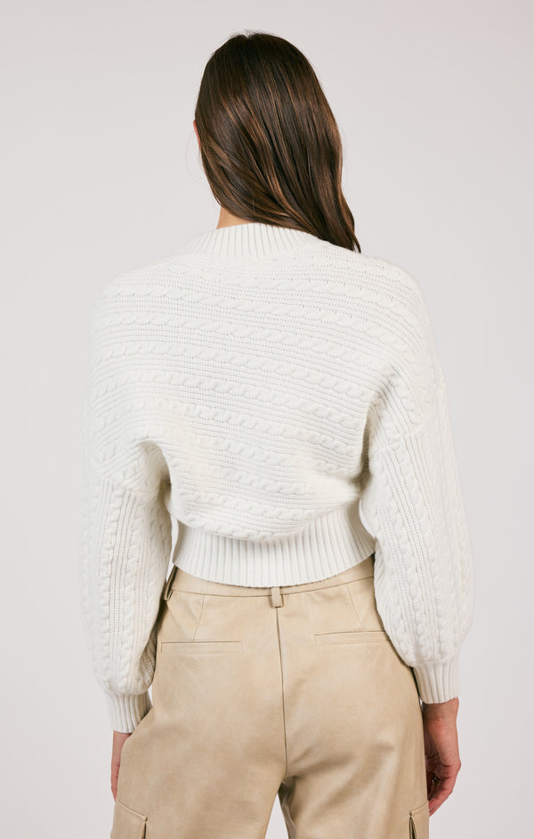 back view of the model wearing the along the vines cable knit sweater. shows the ribbed hems. also shows the cable knit detailing, the dropped shoulders and the exaggerated sleeves.