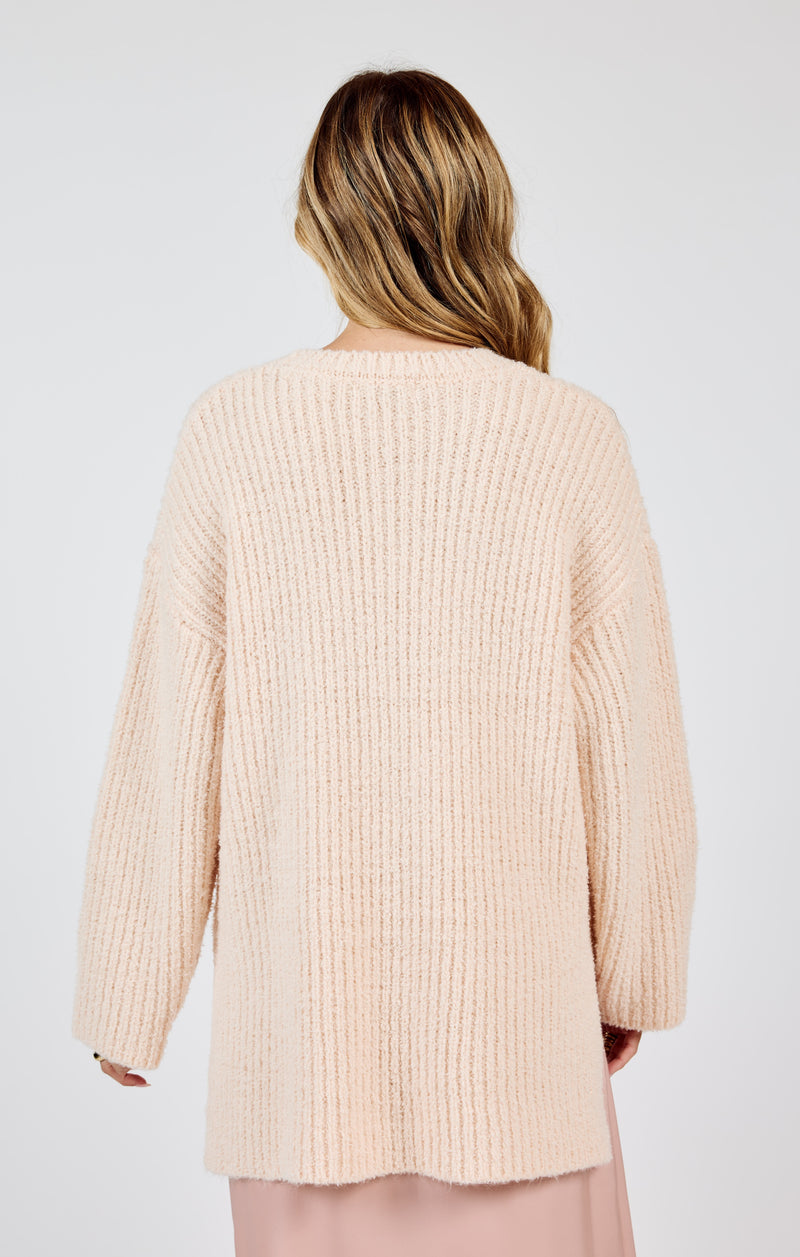 back view of the model wearing the your needs sweater in this cream color. shows the ribbed detailing. also shows the oversized fit, the dropped shoulders. 